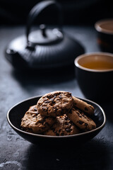 Chocolate chip cookies with tea in background in a dark moody atmosphere 