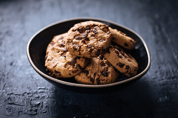 Chocolate chip cookies with tea in background in a dark moody atmosphere 