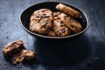 Chocolate chip cookies with tea in background in a dark moody atmosphere 