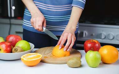 A young girl cuts an orange for making fresh juice. Healthy food concept.