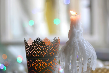 Two candle holders with lit candles and colorful Christmas lights in the background. Selective focus.