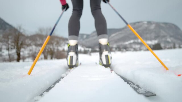 SLOW MOTION, LOW ANGLE, CLOSE UP, DOF: Woman nordic skiing pushes off her poles and skis along two tracks running around the Olympic training center. Unrecognizable female athlete trains nordic skiing