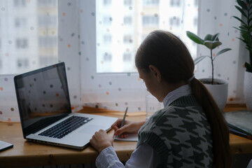 Teenage girl looking at a laptop and doing homework, remote learning