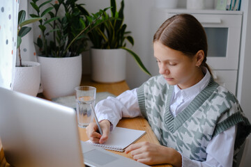 Teenage girl looking at a laptop and doing homework, remote learning