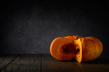 large ripe pumpkin with pulp on a wooden table on a dark gray rough background with a light spot. Thanksgiving Day motives. simple moody still life in rustic style with copy space