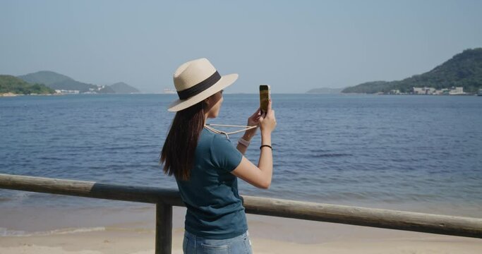 Woman use cellphone to take photo at beach