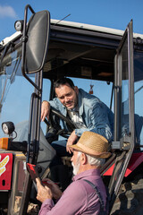 Naklejka premium Two farmers talking beside tractor in field