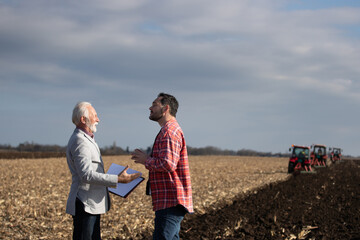 Businessman and farmer talking in field while tractors working