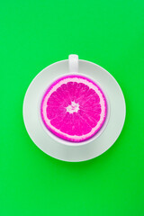 Creative food collage.White tea cup with pink chopped orange on the green background. Top view. Location vertical.