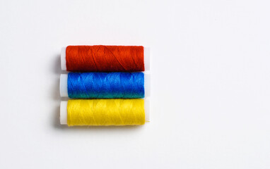 Multi-colored spools of thread for sewing are stacked in the form of the flag of Armenia on a white background. There is a free empty space.