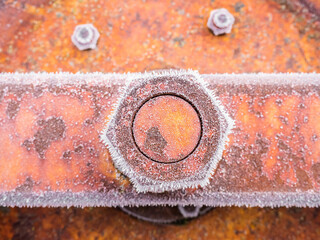 Nut tightened into an orange piece of metal and completely frozen on a winter morning on a grungy...
