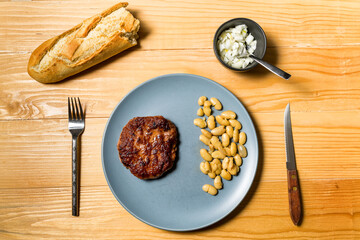 Tasty grilled burger served with coocked vegetarian beans in a plate on a rustic wooden table. Flat lay, top view