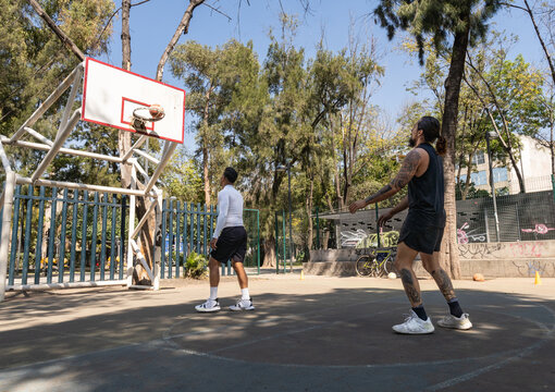 Encestando bal&oacute;n en pr&aacute;ctica de baloncesto entre dos jugadores latinos en cancha de la Ciudad de M&eacute;xico