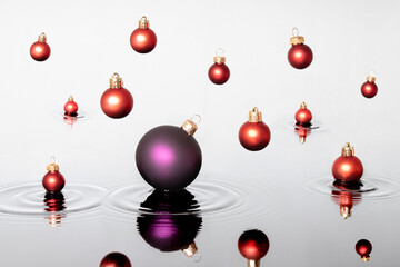 Colorful Christmas ball fall on the water like a rain. Red baubles touches the surface of the water and making waves. Creative New Year minimal concept.