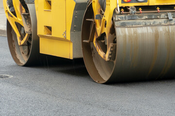 Laying of new modern asphalt. Asphalt laying equipment works on the site. A yellow asphalt skating rink rides in close-up on a new roadbed.
