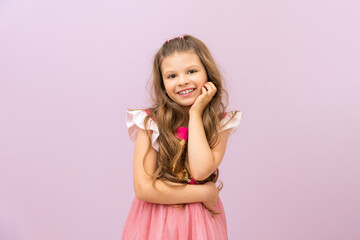 A beautiful little girl in a pink dress and curly hair on a purple isolated background. Copy space.
