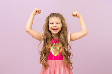 A little beautiful girl shows her strong biceps on a pink isolated background.