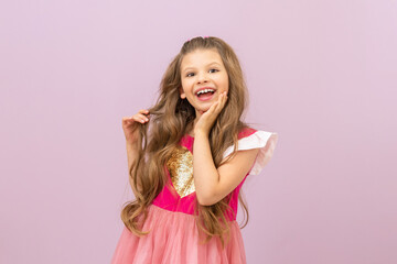 The little girl fluffs her curly, luxurious hair and smiles broadly. Isolated pink background.