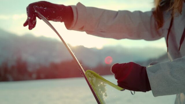 SLOW MOTION, CLOSE UP, LENS FLARE, DOF: Active tourist rips skins off the bottom of their split boarding gear before riding at sunrise. Split boarder takes the protective layer off the bottom of skis.