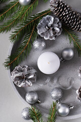 Flat lay out concrete tray with candle, pine cones, spruce branches, silver Christmas balls on gray background. Top view. Vertical photo