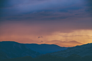 Atmospheric landscape with silhouettes of mountains with trees on background of vivid orange blue violet dawn sky. Colorful nature scenery with sunset or sunrise of illuminating color. Sundown paysage