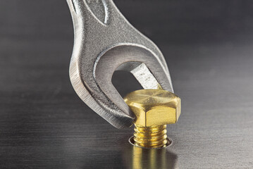 Wrench tightens brass bolt in steel billet. Spanner, bolt, screw and nuts.