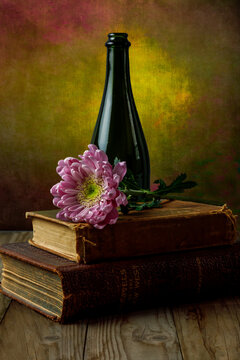 Still Life Of Antique Books, Flower, And Wine Bottle Against Textured Background