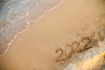 2022 numbers are written on sand on sea beach. New Year 2021 is coming concept. Background for New Year's 
