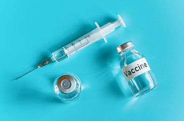 Glass vials with label vaccine and hypodermic syringe needle near, view from above on cyan...