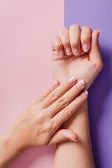 Close-up of woman's hands with French manicure on purple and salmon background.