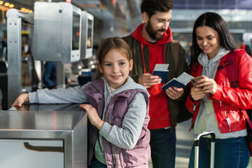 Happy little girl standing at the airport with her parents while they checking tickets details at...