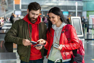 Happy woman pointing with finger while standing together at the airport and checking tickets...