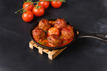 Stewed meatballs in tomato sauce in a pan on a dark background.
