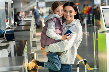 Waist up portrait view of the overjoyed mother and daughter embracing with each other after giving documents to airport worker