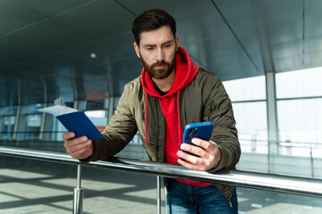 Waist up portrait of the young caucasian man standing at the airport lounge and checking his...