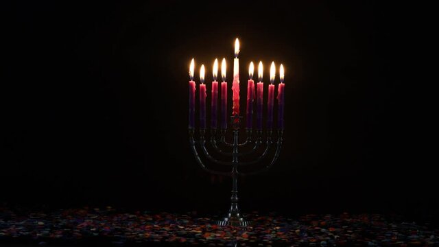 Burning menorah with pink candles and confetti on black background. Jewish holiday Hanukkah symbol.