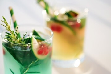 Mojito, fresh alcoholic green cocktail or lemonade with lime,red berries, ice and rosemary in glasses. .Summer vocation concept.top view.Sun and shadows.Close up