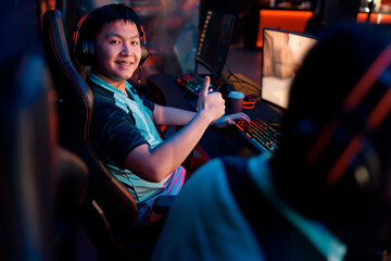Asian professional cybersport gamer happy with his game while showing thumbs up sign in interior of gaming club