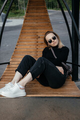 Young beautiful white girl is sitting on a park bench. Cute female lifestyle, portrait with soft focus. thoughtful stylish girl with a thoughtful calm face poses outdoors. Cute stylish woman