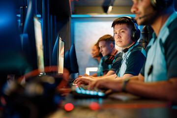 Team of professional esports gamers with concentrated Asian man in focus playing in video games on...