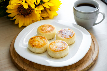 Portion of four sweet cheese pancakes on plate with sunflowers on background of kitchen. Homemade good morning snack of traditional Russian curd fritters.
