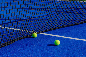 Two balls next to the net of a paddle tennis court. Racket sport concept.