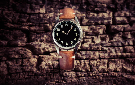 Wind-up watch with black dial and vintage-style honey-colored strap on old cracked wooden trunk.