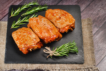 Raw chicken meat.Chicken thighs marinated in red sauce on a kitchen ceramic board with rosemary leaves.
