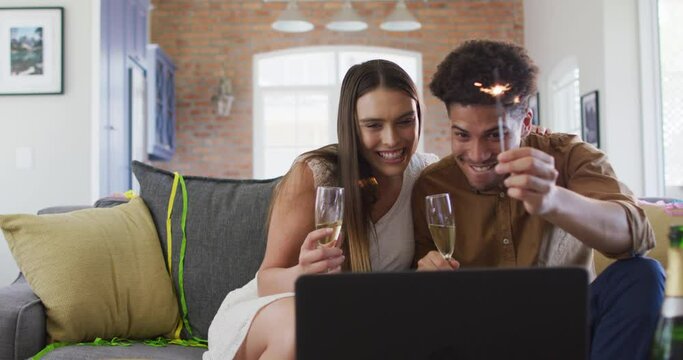Happy biracial couple drinking champagne at home making celebration laptop video call and laughing