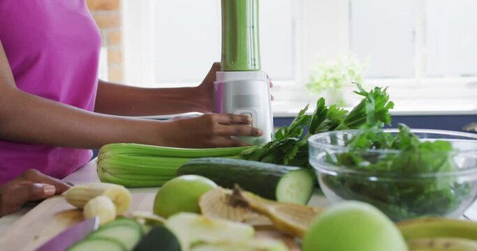 Midsection of african american mother and daughter preparing healthy drink in kitchen