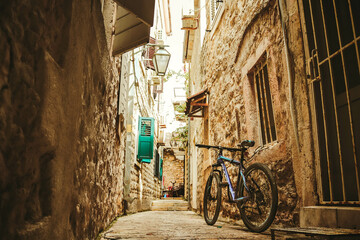 Cozy narrow Roman street in the city of Budva. Old bicycle, street lamp, wooden shutters. Retro, vintage. Montenegro, Balkans. Summer.