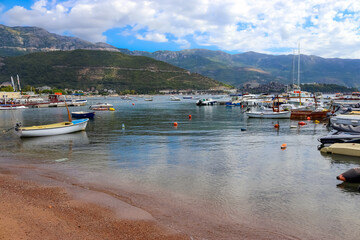 Beach and pier in Budva, Montenegro, Balkans, Adriatic Sea. Yachts and boats in the bay. Mountains and clouds.