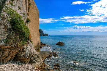 Beautiful sea view in the city of Budva. Old stone wall with moss, stones, sky with clouds. Montenegro, Balkans. Summer.