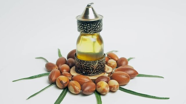 Argan oil in a oriental glass and metal bottle and argan nuts with green leaves motion on white background.